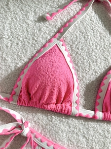 Close-up of pink smocked bikini top with white scalloped trim on white plush background