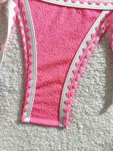 Detail of bright pink ruched bikini bottom with white ties and triangle embroidery