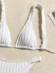Close-up of white crinkle seersucker bikini top texture on beige woven background