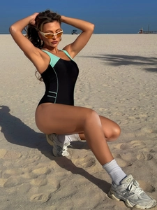 Detail of black one-piece swimsuit with mint green side straps and waist cutout details