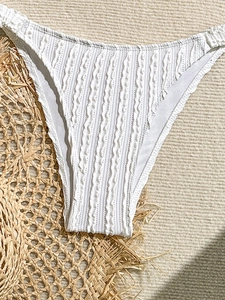 Detail of white textured bikini bottoms with ruffled edges and high cut design on straw mat