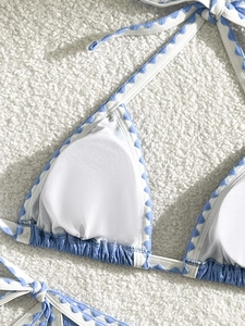 Blue and white bikini top with scalloped edges and ties on a soft white background