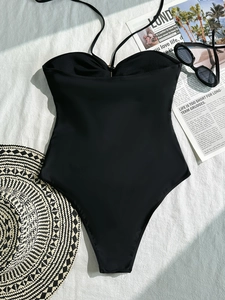 Black halter one-piece swimsuit with neck ties, straw hat, and sunglasses on white linen