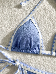 Light blue crinkle fabric bikini top with printed white trim on a plush background