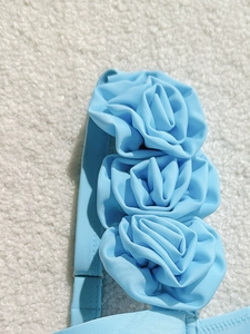 Detailed close-up of light blue fabric straps featuring three large handmade 3D floral rosettes