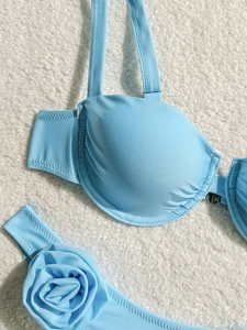 Close-up of light blue bikini featuring a 3D floral accent and pleated fabric texture