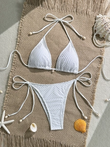 Detailed macro view of white crochet bikini with shell accents and mesh texture on sand mat