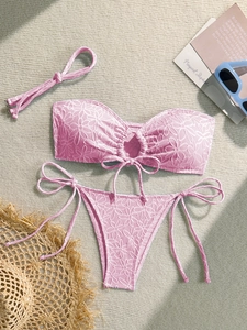 Detailed flat lay of a pink textured bikini with floral embroidery and side tie details