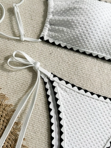Close-up of white waffle texture bikini fabric with black ric-rac trim and side ties