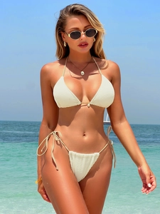 Three-piece beige textured bikini set with shell charms on a sunny beach background