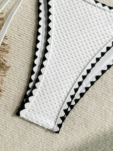 Detail of white waffle texture bikini bottom with black scalloped edge and side ties