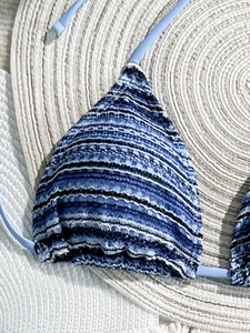 Detail of blue striped crochet bikini top with textured fabric on straw hat background
