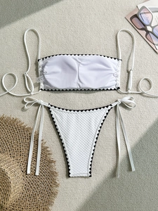 Flat lay detail of a white waffle textured bikini with black scalloped edge and tie sides