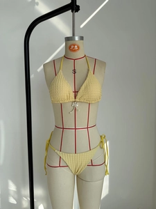 Detalle del bikini amarillo con textura tejida y colgante de lazo de perlas