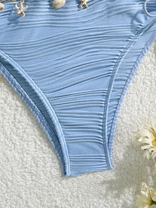 Dettaglio del slip bikini azzurro con texture a costine e decorazioni a forma di conchiglia
