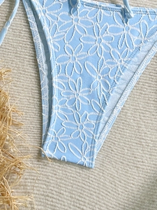 Blue bikini bottom with 3D floral texture and side tie straps on natural beach background