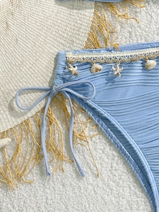 Dettaglio slip bikini azzurro testurizzato con pizzo bianco e ciondoli a conchiglia