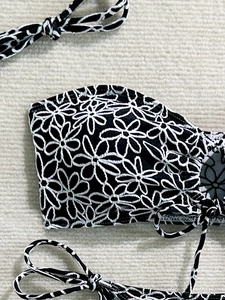 Detail of black bikini top featuring white daisy embroidery and scalloped edges
