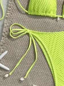 Detail of neon green mesh bikini with white shell accents on brown woven beach mat