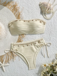 Vista piatta di bikini color crema con dettagli di conchiglie e stelle marine sui bordi