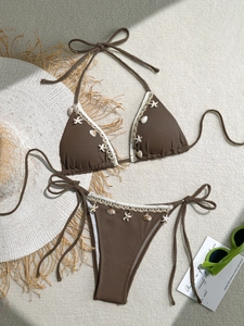 Flat lay of brown textured bikini with white lace trim and seashell charms on a neutral rug