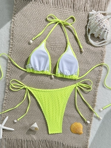 Detail of neon green textured bikini with decorative shells on a summer beach mat