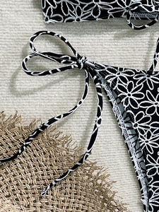 Detail view of daisy print bikini bottom with side tie strings on a beach mat