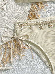 Dettaglio slip bikini beige con tessuto testurizzato e ciondoli a conchiglia e stella