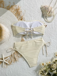 Bikini crema con bordo in conchiglia e trama a onde su sfondo bianco morbido