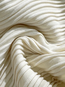 Dettaglio del tessuto plissettato bianco crema con trama a costine e finitura in velluto