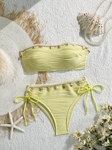 Dettaglio di un bikini a fascia con trama a onde e ciondoli a conchiglia e stella marina