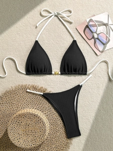 Detail of black ribbed bikini set featuring white ties and golden shell charm ornament