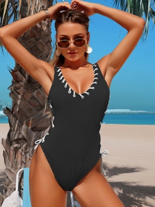 Detail of black ribbed one-piece swimsuit with white lace-up sides against a beach background