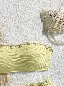 Dettaglio del top bikini a fascia giallo a coste con conchiglie e bordo in pizzo