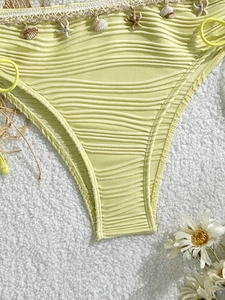 Dettaglio slip bikini verde chiaro a coste con ciondoli a conchiglia e stella marina