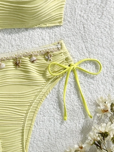 Dettaglio del tessuto a onde con ciondoli a conchiglia e stella marina sullo slip bikini