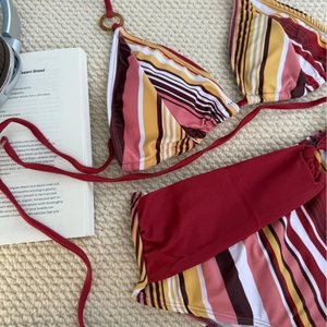 Flat lay of retro striped two-piece bikini with gold ring detail on textured fabric