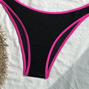 Macro detail of black crinkle bikini bottom with pink piping and textured fabric