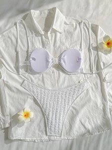 Flat lay of white seersucker bikini with lace trim and plumeria flowers on beach shirt