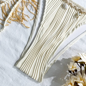 Detailed macro view of beige ribbed bikini bottom with woven shells and starfish charms