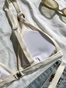 Cremefarbenes Ripp-Bikini-Oberteil mit Bernsteinring auf natürlichem Leinenhintergrund