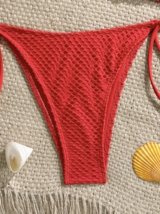 Detailed macro view of the intricate red crochet mesh texture on bohemian bikini bottoms