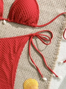 Close-up of red crochet bikini texture with small white seashell accents on woven mat