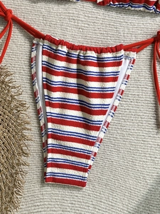 Detail of red and blue striped bikini bottom with side ties on a woven beach mat