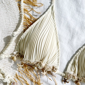 Macro shot of cream bikini top featuring vertical pleats and decorative sea shells