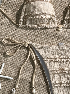 Detailed view of beige textured bikini with tiered ruffles and shell accents on flat lay