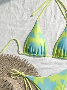 Flachbild-Foto eines Tie-Dye-Marmor-Bikini-Sets mit Strohhut auf weißem Stoff
