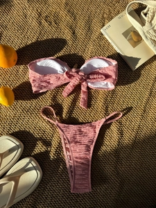 Close-up of pink ruched bikini with bow detail on beach vacation straw mat setting