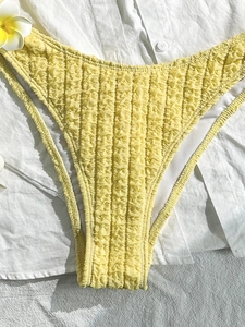 Smocked bright yellow bikini bottoms with sunflower petal texture on white linen background