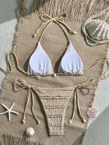 Detail of white bikini top with ruffled texture, shell charms, and seaside beach props